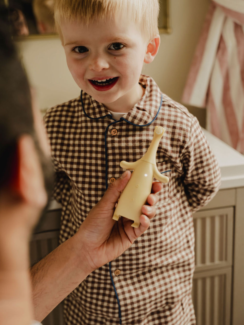Child holding a Brushi Bear electric toothbrush while standing next to an adult in a home setting