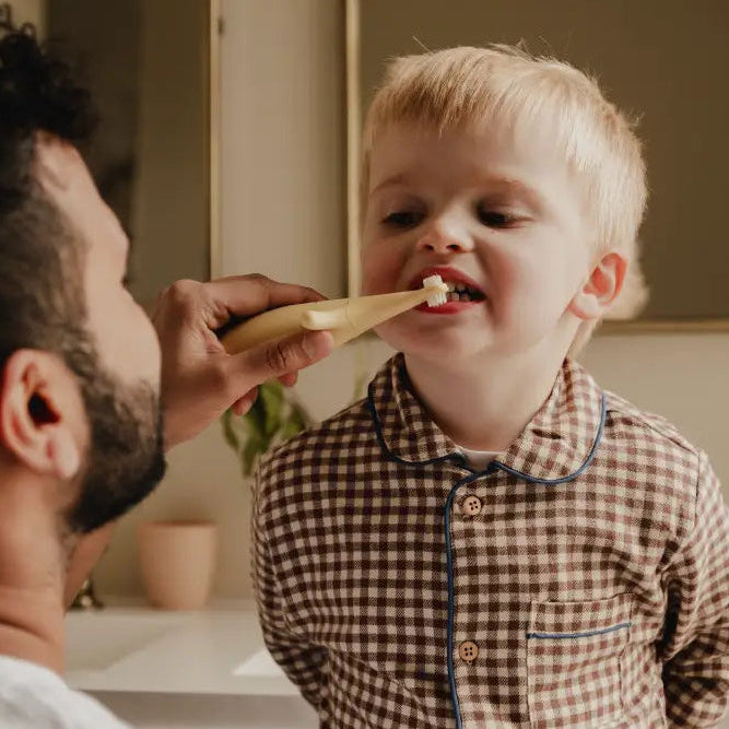 Dad teaching a child how to brush teeth using  Brushi Bear™ in a bathroom setting